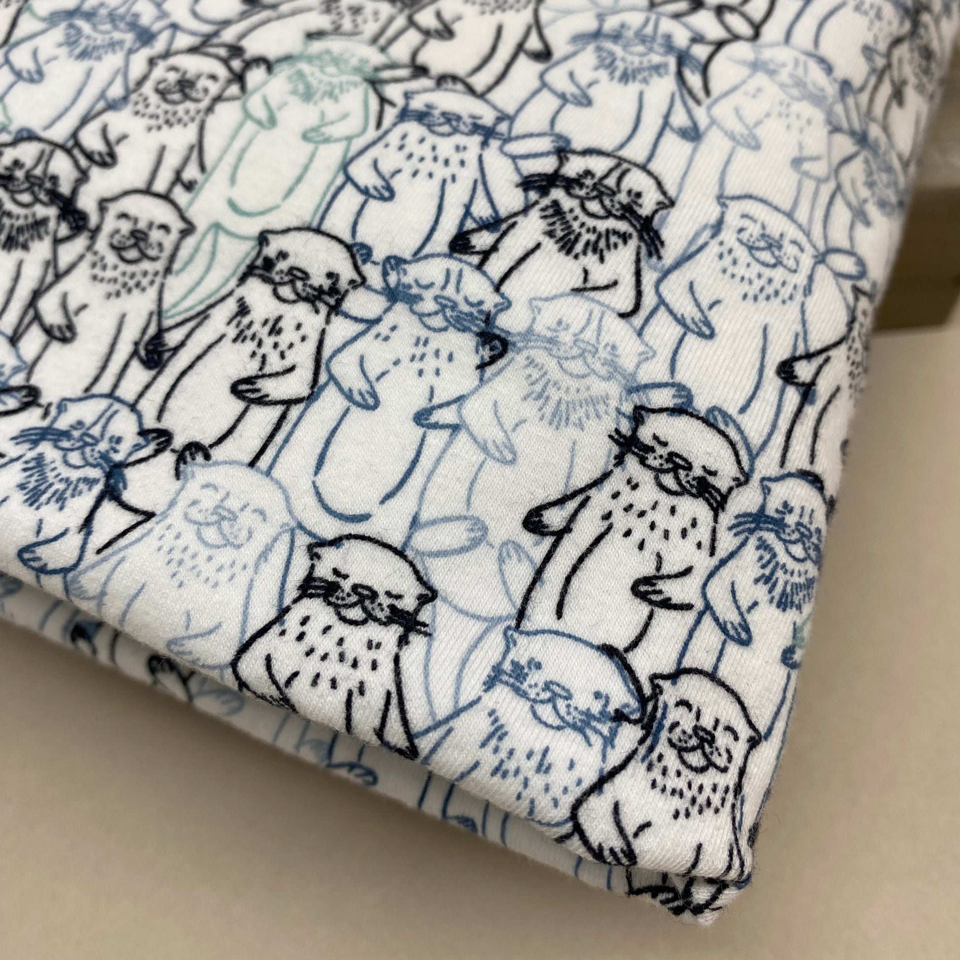 A close-up of folded fabric with a white base printed all over with cartoon seals in blue and black line art.